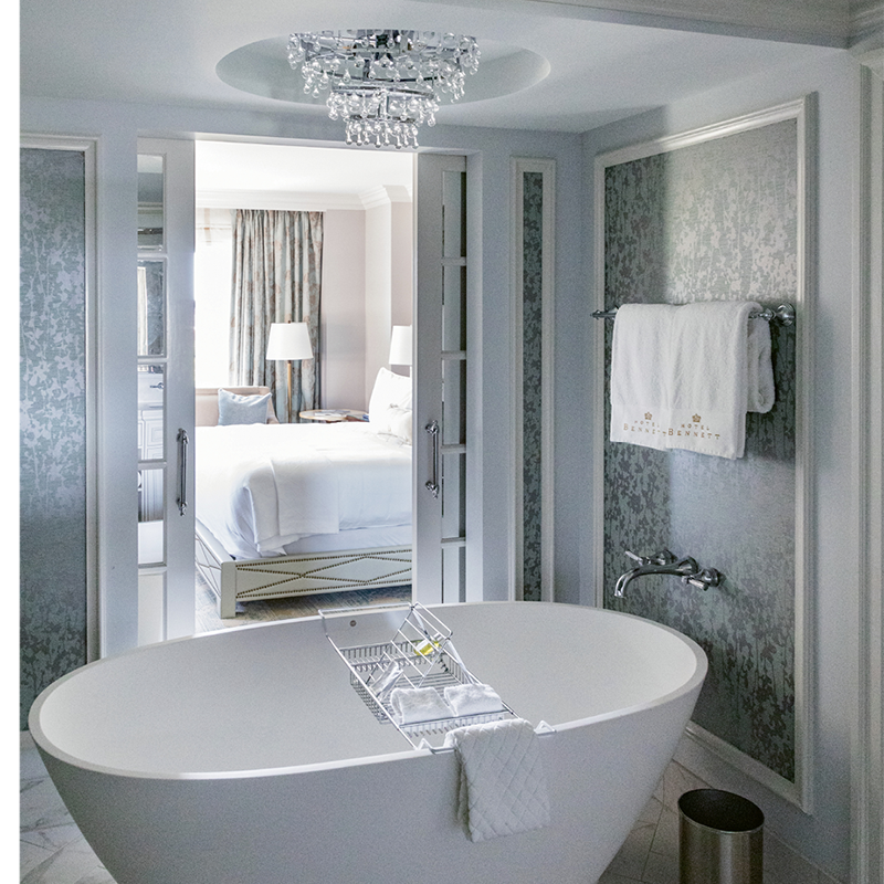 In a light-filled guest room, French doors slide open to reveal a marble-clad spa-like bath, complete with deep pedestal tub. 